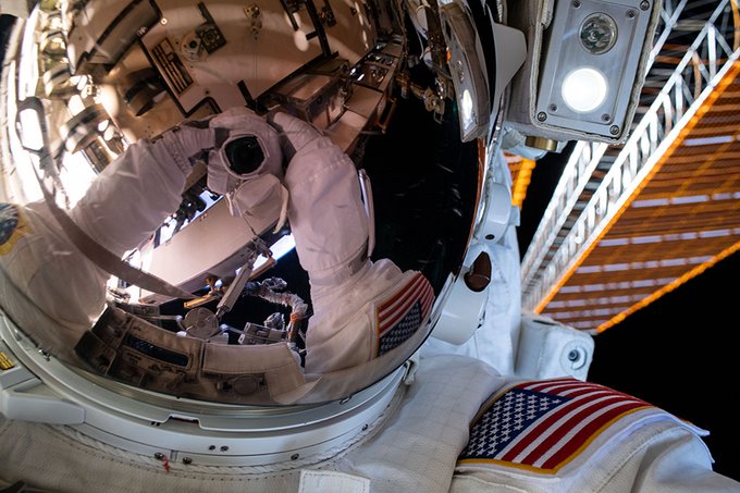 NASA astronaut Bob Behnken's spacesuit gloves and camera are reflected in his helmet's visor in this