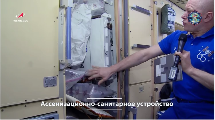 Олег Новицкий показывает кабину туалета, которую освобождают от грузов к прилету нового экипажа. Фото: ЦПК/Роскосмос height=100% width=100%