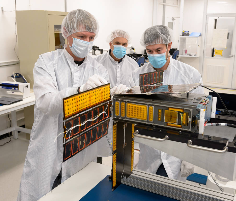 Researchers perform a solar array deployment and gimbal motion test on the spacecraft in a clean room.