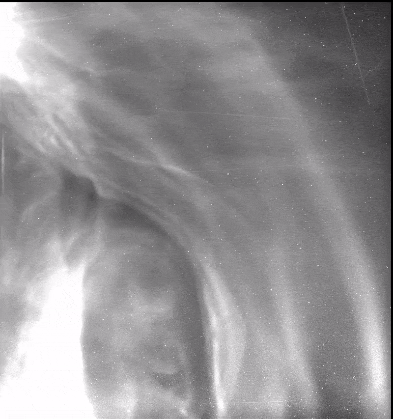 In black and white, a cloud from a CME pushes the bright speckles of dust out of the way, leaving a screen of near darkness.