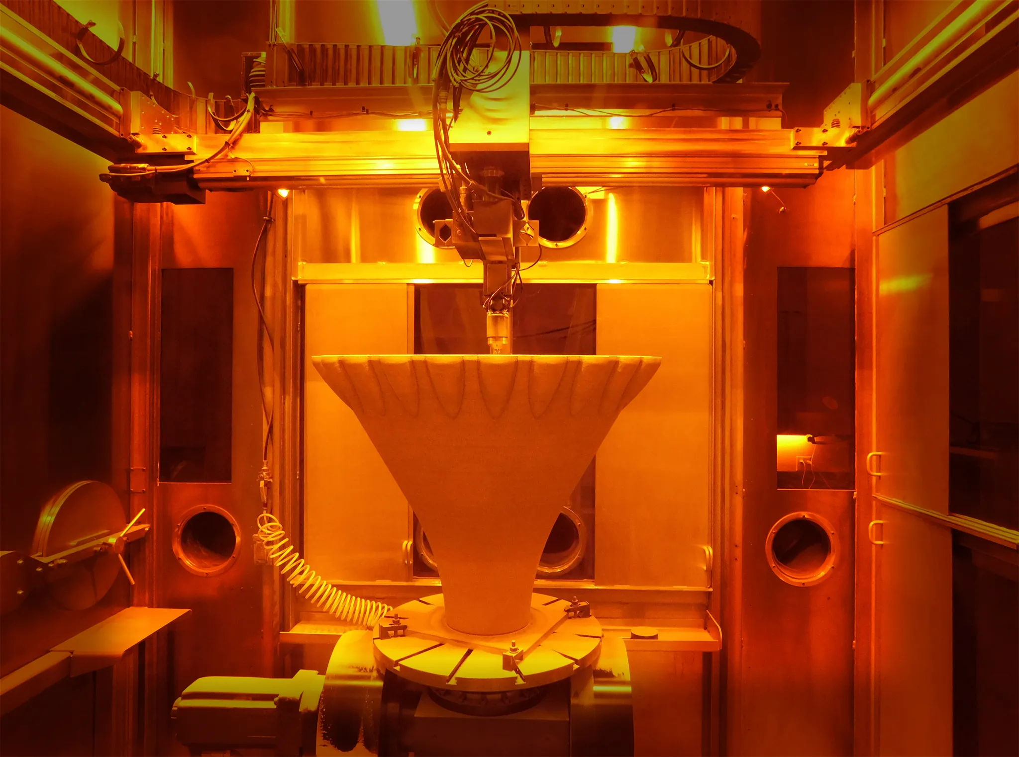 A nozzle is being created by a 3D printer layer by layer. The photo has a golden hue from the light and laser.