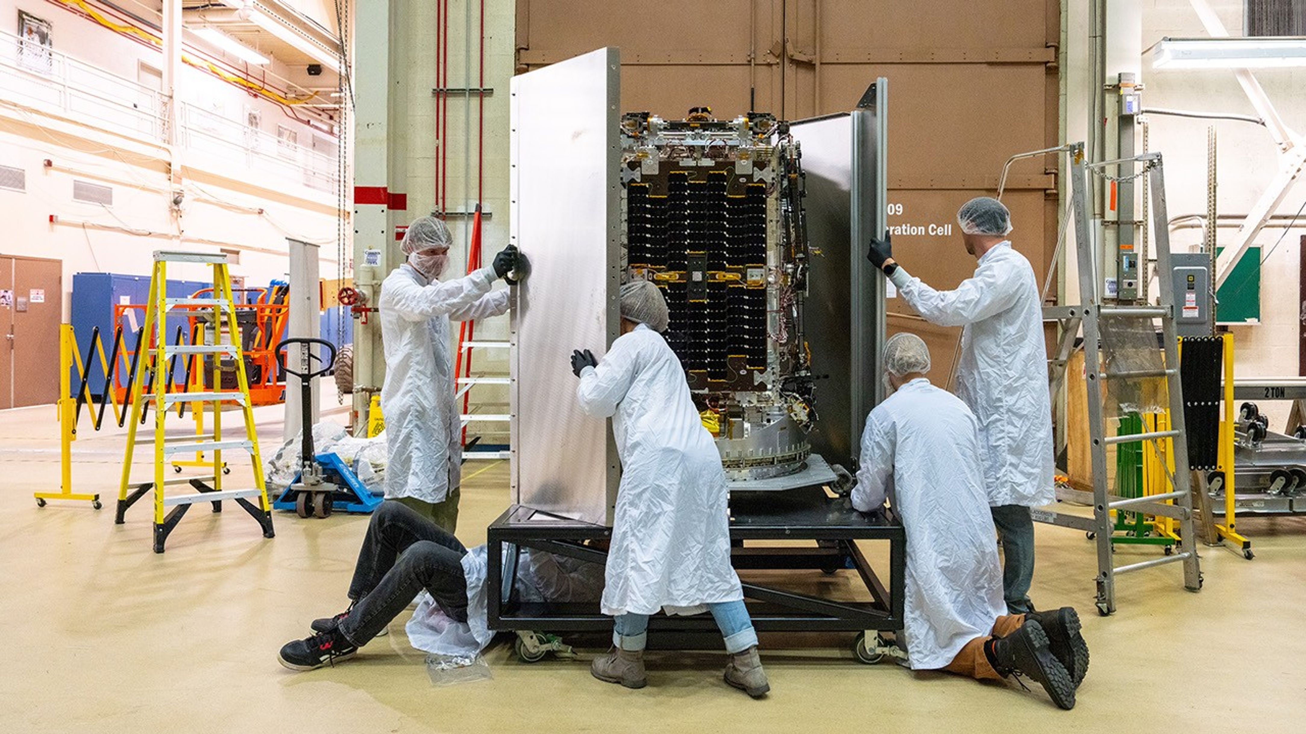 Engineers in clean suits unbox a satellite.
